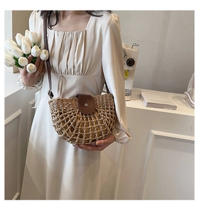 Detail of a half-moon straw crossbody bag with brown leather flap and hollow weave texture