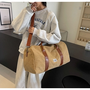 Large khaki canvas travel bag with leather straps worn as a crossbody messenger bag