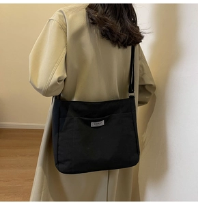Detail view of the black canvas tote bag featuring an adjustable strap and white brand label
