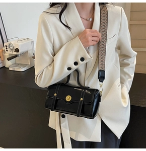 Close-up of black glossy leather crossbody bag with golden twist lock and jacquard strap