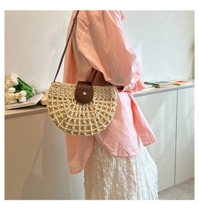 Detail of half-moon straw bag with brown leather flap worn by model in a cozy indoor setting