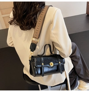 Close-up of black glossy leather crossbody bag featuring a patterned wide woven strap