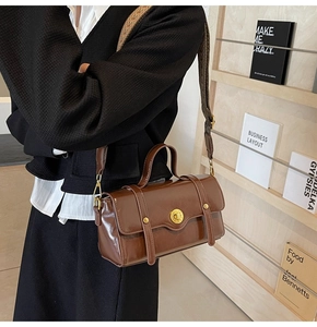 Detail of brown glossy leather crossbody bag with woven strap and gold round lock