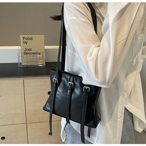 Détail d'un sac cabas noir brillant avec trois boucles argentées pour un style rétro chic