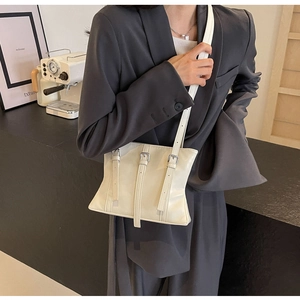 Détail du sac fourre-tout blanc crème avec trois sangles à boucles sur un blazer gris