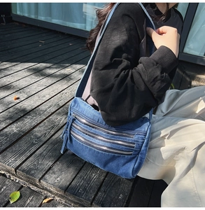 Close-up of blue denim crossbody bag with three silver zipper pockets and adjustable strap
