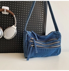 Close-up of denim tote bag featuring three functional front zippers and long strap detail