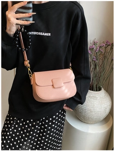 Close-up of pink lychee leather crossbody saddle bag with gold hardware on a model