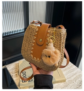 Detail of straw woven bucket bag with brown leather flap and a cute teddy bear charm