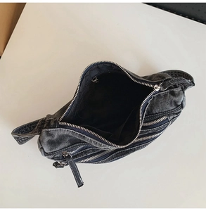 Detail view of washed denim crossbody bag featuring multiple zippers and internal storage