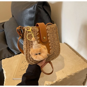 Close-up of hand-woven straw bag with leather flap and cute bear pendant on stone slab