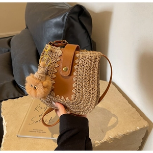 Detail of woven straw shoulder bag with brown leather flap and cute teddy bear charm