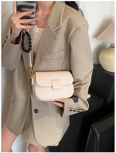 Close-up of beige lychee leather crossbody bag with square clasp and beaded accessory