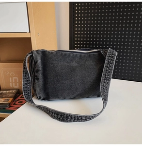 Detail view of a retro dark gray denim tote bag with zipper closure on a white table