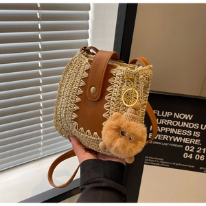 Close-up of beige woven straw shoulder bag with brown leather flap and cute plush charm