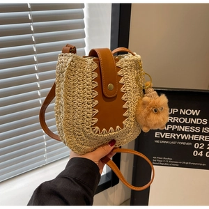 Detail of woven straw shoulder bag featuring brown leather trim and cute plush charm