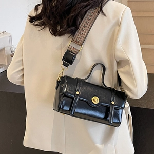 Black leather crossbody bag with wide woven strap and gold buckle shown on a model