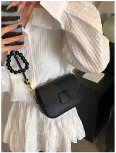 Detail of black pebble grain bag with oversized bead handle worn with white dress