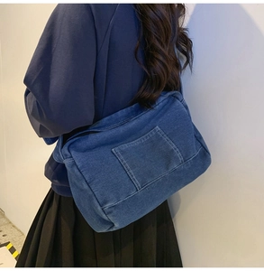 Détail d'un sac bandoulière en denim bleu foncé avec coutures contrastées et poche frontale