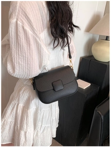 Detail of black pebble leather crossbody bag with gold hardware on a model