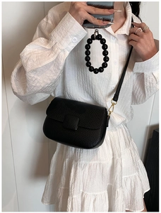 Detail of black lychee grain leather crossbody bag with elegant gold metal buckle