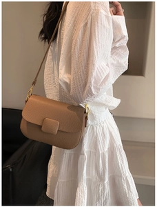 Brown lychee leather saddle bag shown on a model with golden buckle and crossbody strap