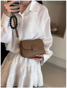 Detail of a brown lychee-patterned leather crossbody bag worn on a white outfit