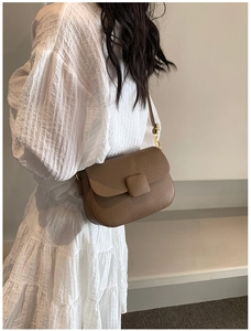 Brown lychee leather saddle bag with gold hardware shown on model in white dress
