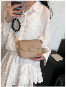Detail view of a beige crossbody bag with lychee texture and golden hardware accents