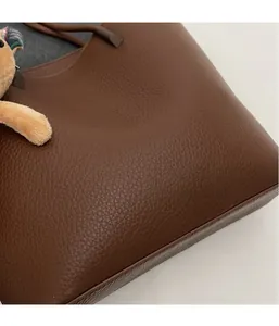 Detail of brown litchi pattern leather tote bag with plush bear charm and stitching