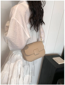 Detail view of beige lychee pattern crossbody bag with square buckle on model's back