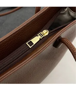 Macro detail of golden metal zipper and smooth hardware on brown pebbled leather bag