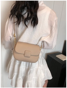 Close-up of beige lychee grain leather saddle bag with elegant gold metal hardware buckle