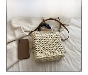Detail view of woven straw beach bag featuring wooden handles and leather shoulder strap