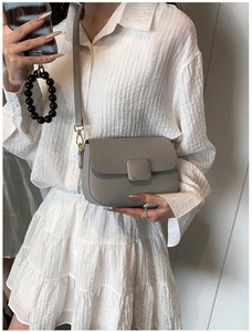 Detail of light grey lychee leather crossbody bag with golden hardware and square buckle