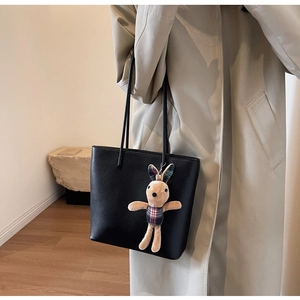 Close-up of black pebble leather tote bag with a beige plaid rabbit plush keychain