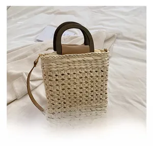 Detail of woven straw bucket bag with dark brown wood handle and slender strap