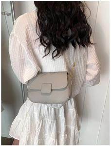 Detail of grey lychee texture leather crossbody bag with metallic clasp and strap