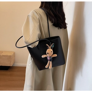 Minimalist black tote bag in litchi leather with a cute plush bunny charm on shoulder