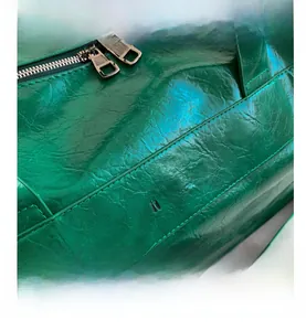 Detail of green glossy wrinkled leather bag with silver zippers and embossed logo