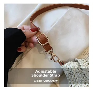 Nahaufnahme des verstellbaren braunen Leder-Schultergurts mit goldener Hardware an Strohtasche