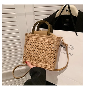Close-up of woven straw bucket bag with dark wood handle and slim leather shoulder strap