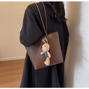 Detail of brown pebbled leather tote bag with a cute plush bunny charm on the shoulder strap
