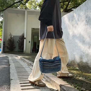 Blue denim tote bag with triple silver zippers shown in a casual outdoor street style setting