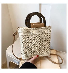 Detail of hand-woven straw bag with round wooden handles and adjustable leather strap