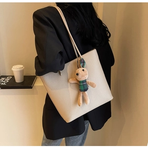 Side view of beige textured tote bag with cute plush bunny pendant and slim shoulder strap