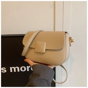 Close-up of beige lychee-patterned leather crossbody bag with golden metal hardware
