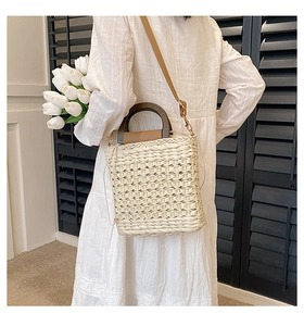 Detail of beige woven straw handbag featuring round wooden handles and leather strap