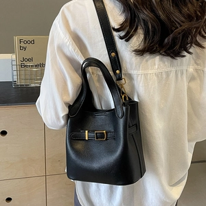 Black lychee leather bucket bag with gold buckle and crossbody strap on shoulder