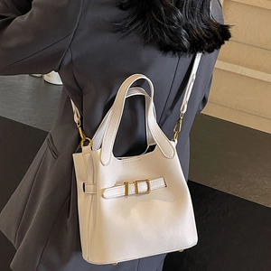 Minimalist beige pebble leather bucket bag with gold hardware shown on a model